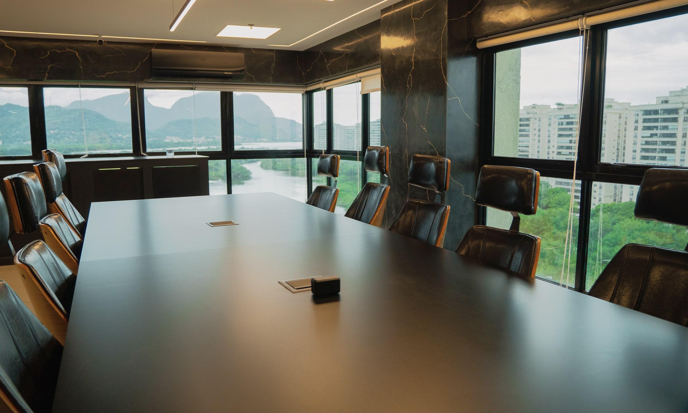 Sala de reunião do escritório, com mesa ampla e janelas voltadas para as montanhas e a lagoa da Barra da Tijuca
