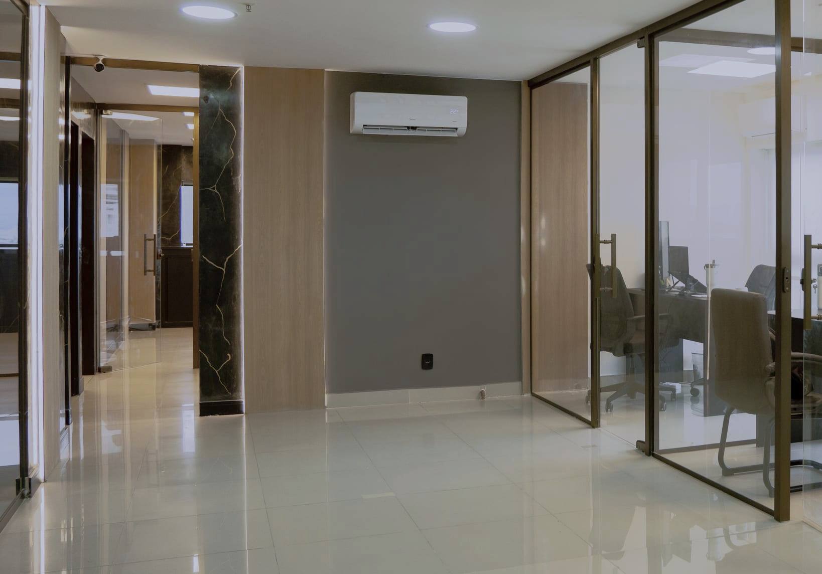 Corredor das salas de atendimento, com divisórias de vidro, portas em perfil dourado e piso claro