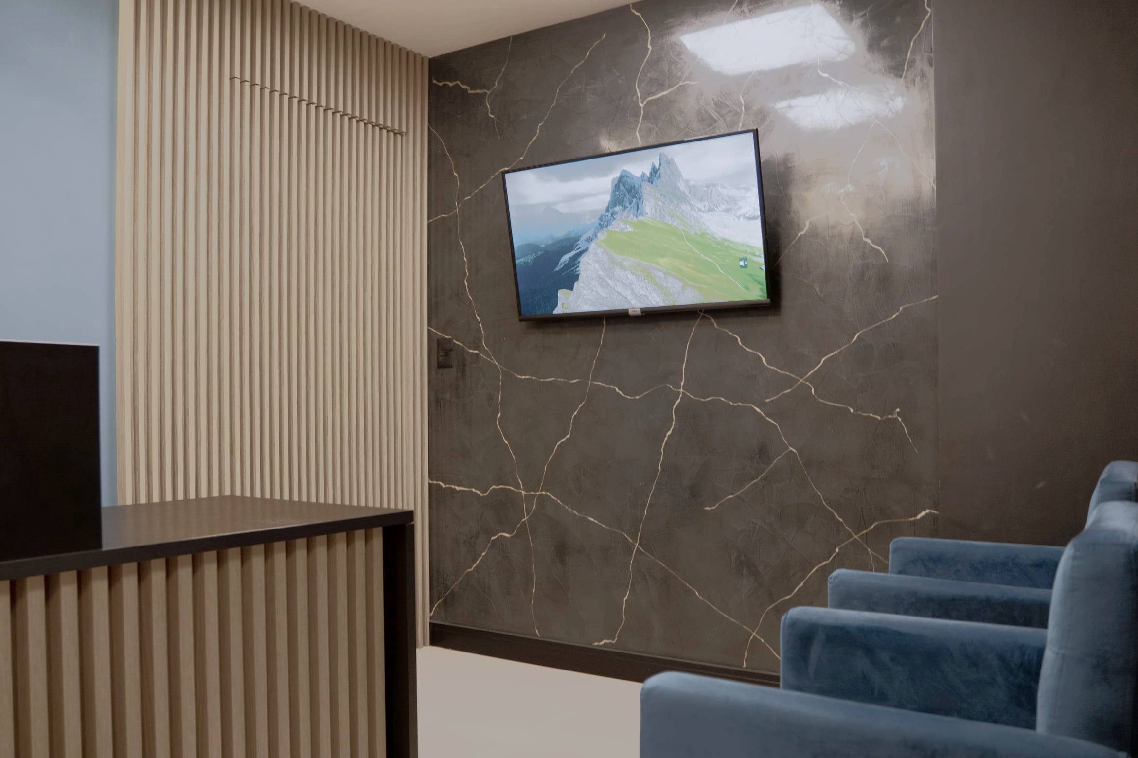 Sala de espera da recepção, com poltronas azuis, parede em pedra escura e painel ripado em madeira clara